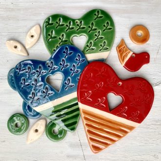 Három kerámia szív: piros, kék és zöld, és az alkatrészeik, amikből összeáll egy-egy ajándék alkotócsomag
