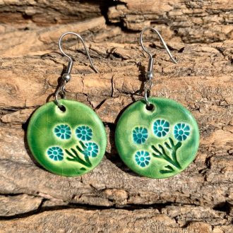 Fa alapon fekszik egy pár kerek, zöld, türkiz virágokkal díszített lógós fülbevaló